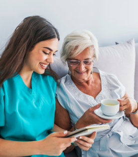 a caregiver woman reading something and an elderly woman holding a cup of coffee